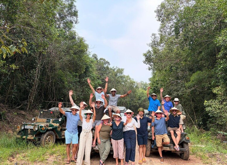 A group of people in a forested area with a vehicle in the background. 1