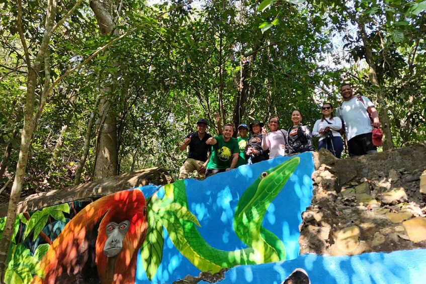 A group of people standing on a rocky path in a forested area with a colorful mural of a gorilla and a snake. 1