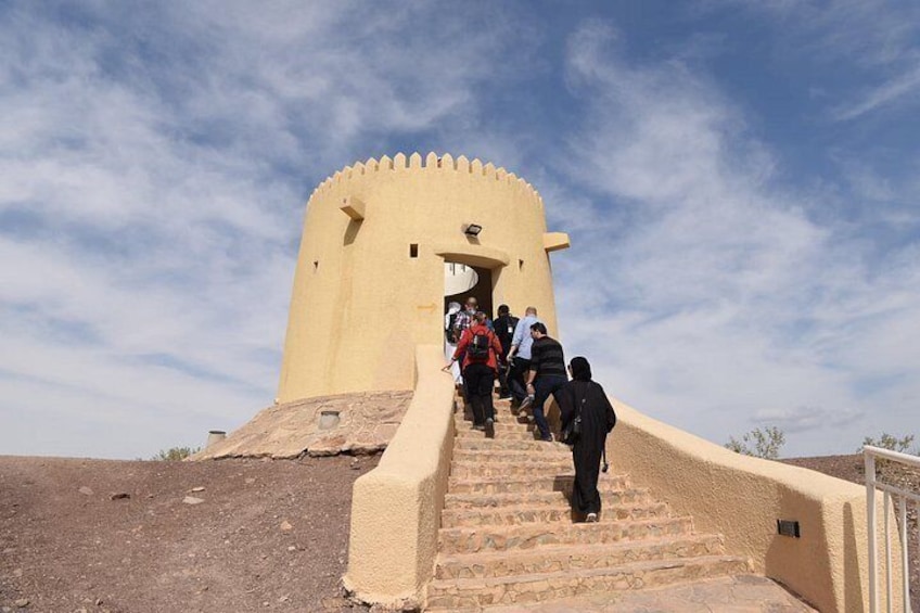 A group of people ascending a set of stone steps towards a yellow tower with a crenellated top. 2