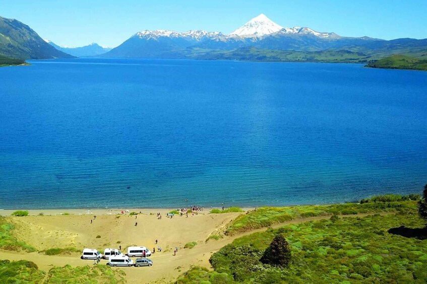 A lake with a mountain in the background and a beach with people and vehicles. 3