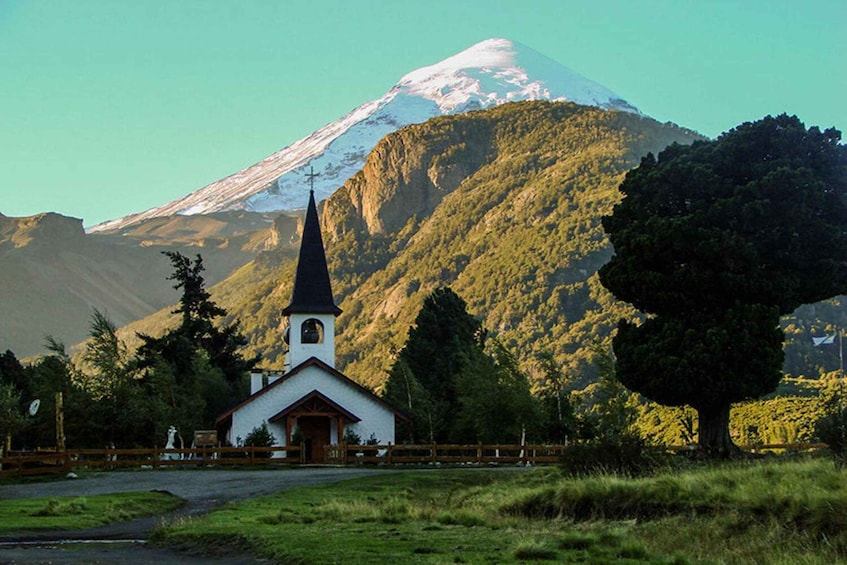 A church with a steeple, a snow-capped mountain in the background, and a forested area. 4