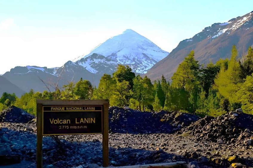 A sign for Volcan Lanin with a view of a snow-capped mountain and a forested area. 5
