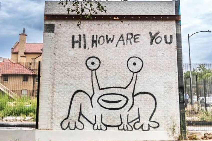 En væg med graffiti, hvor der står 'HI, HOW ARE YOU', og en tegning af et væsen. 3