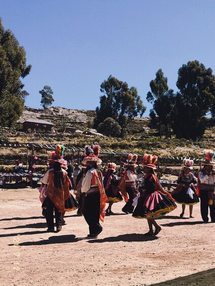 A group of people in traditional attire performing a dance in an open area with a clear sky and a hilly landscape in the background. 2