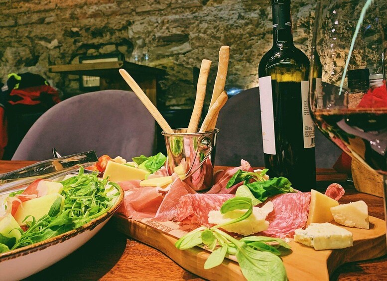 A charcuterie board with various meats, cheeses, and greens, accompanied by a bottle of wine and a glass. 4