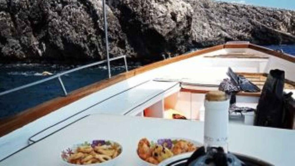 A boat with a table set for a meal, rocky cliffs in the background, and calm water. 5