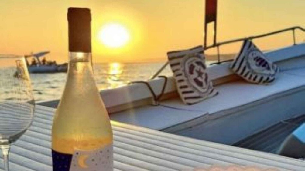A bottle of wine and a glass on a boat deck with a sunset in the background. 3