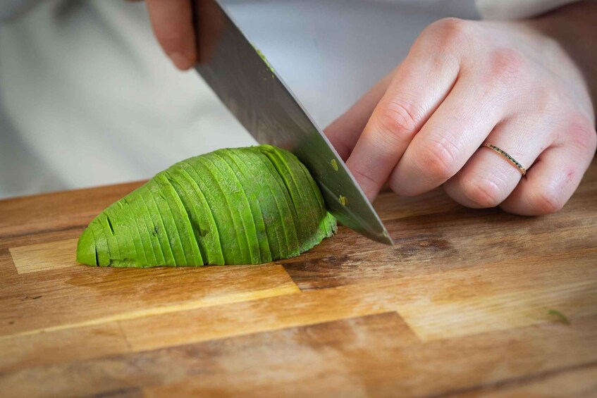 A person slicing a green vegetable on a wooden cutting board. 5