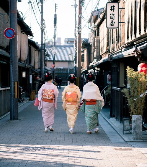 Three women in traditional attire walking down a street lined with buildings. 3