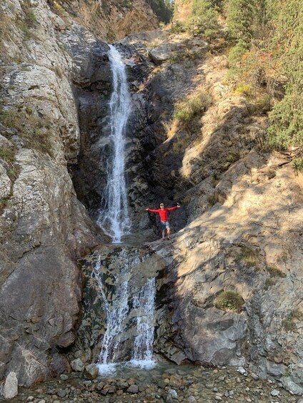 A waterfall in a rocky terrain with a person standing at the base. 4