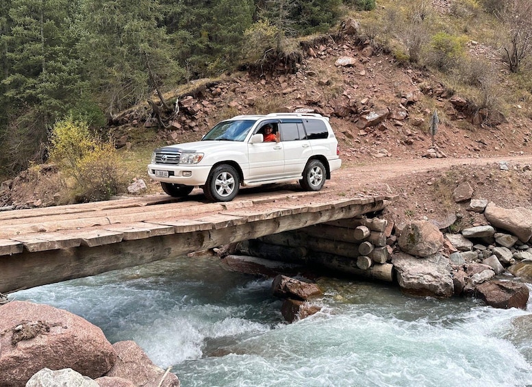 A white SUV crossing a wooden bridge over a fast-flowing river. 2