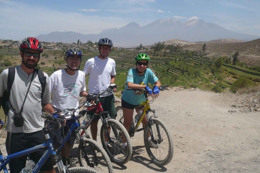 Four cyclists on a dirt path with terraced fields and mountains in the background. 4