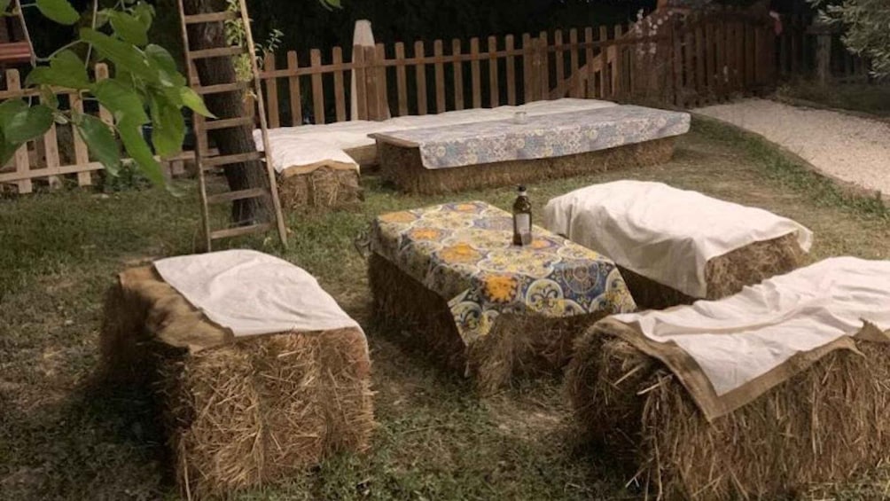 Hay bales arranged in a garden with a wooden fence and a table with a patterned tablecloth. 5