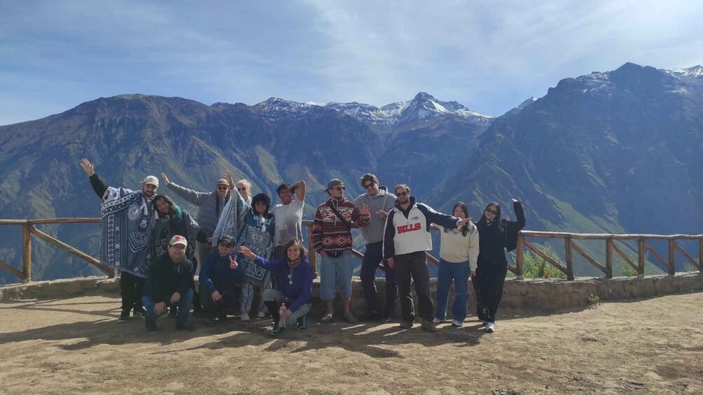 A group of people posing on a mountain overlook with snow-capped peaks in the background. 4
