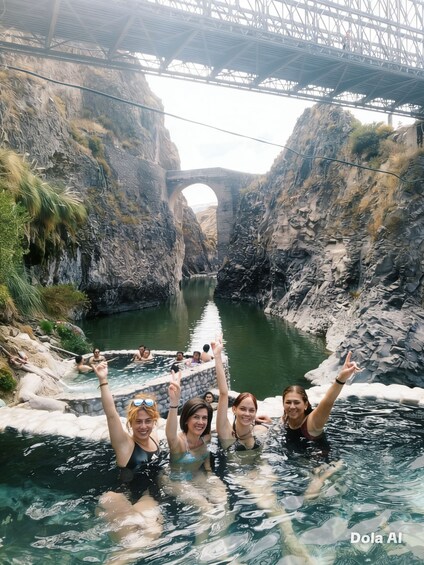 A group of people in a natural hot spring with a bridge in the background. 2