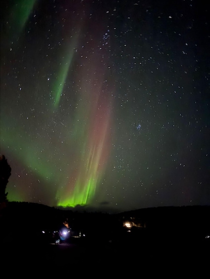 The aurora borealis over a dark landscape with a few distant lights. 4