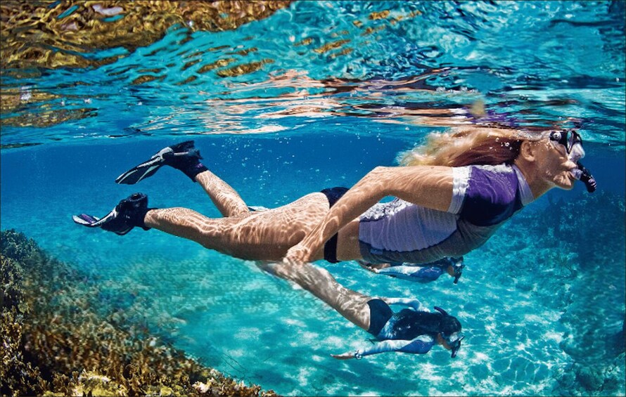 Two people swimming underwater in a clear blue pool. 1