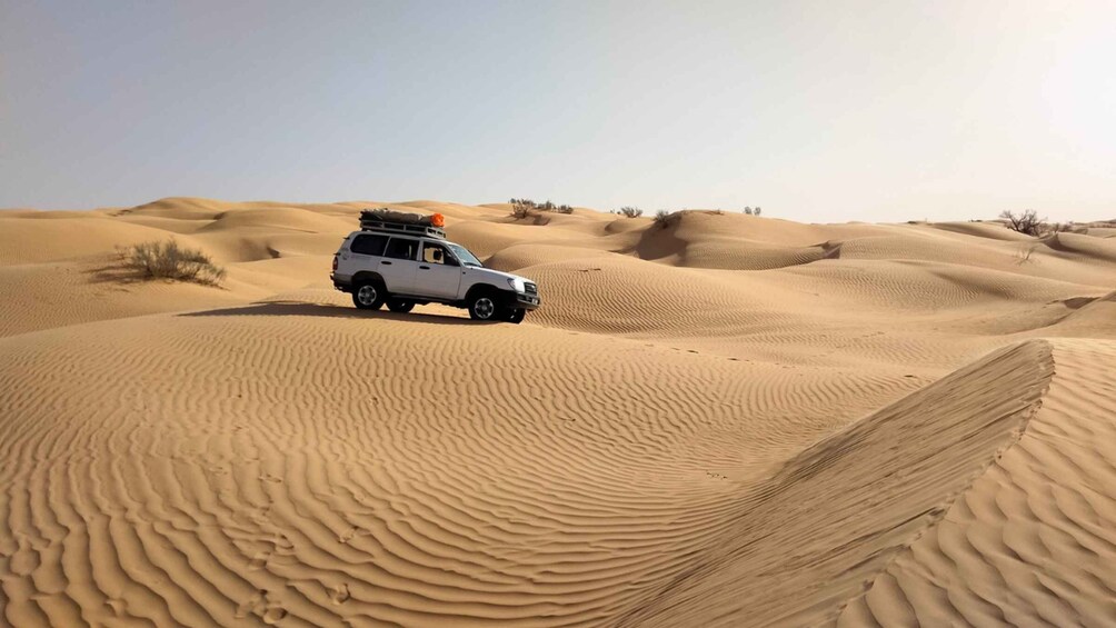 A white SUV in a desert with sand dunes. 1