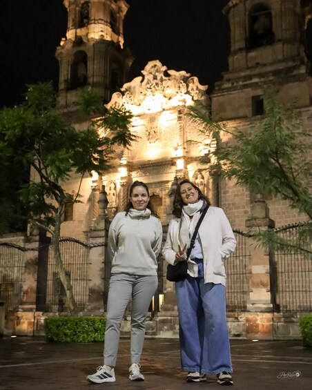 Two people standing in front of a historic building with ornate architecture and a clock tower. 2