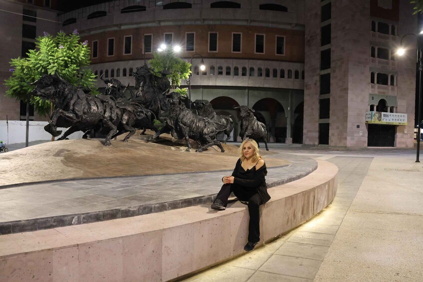 A woman sitting on a curved stone bench in front of a bronze bull sculpture. 2