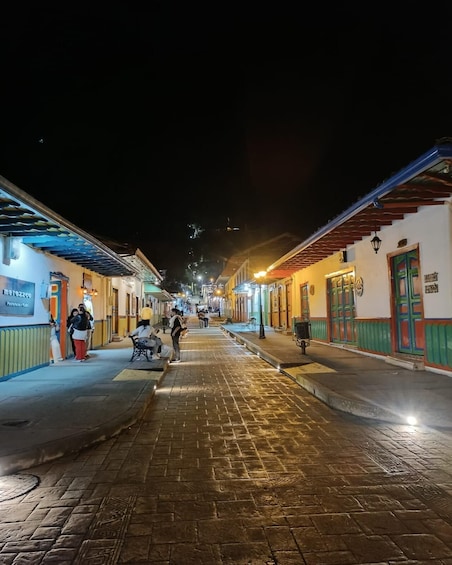 A nighttime street scene with cobblestone pavement, buildings with colorful facades, and people walking and sitting. 5
