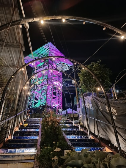 A brightly lit tower with a geometric design, surrounded by a metal structure with lights. 2