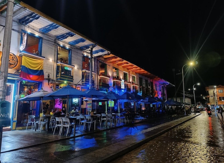 A brightly lit street with outdoor seating and a flag. 1
