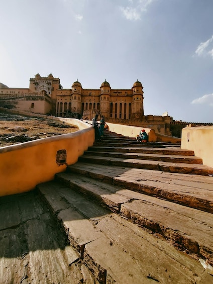 A historic building with arched windows and domed towers, a stone staircase leading up to it, and a clear sky. 5