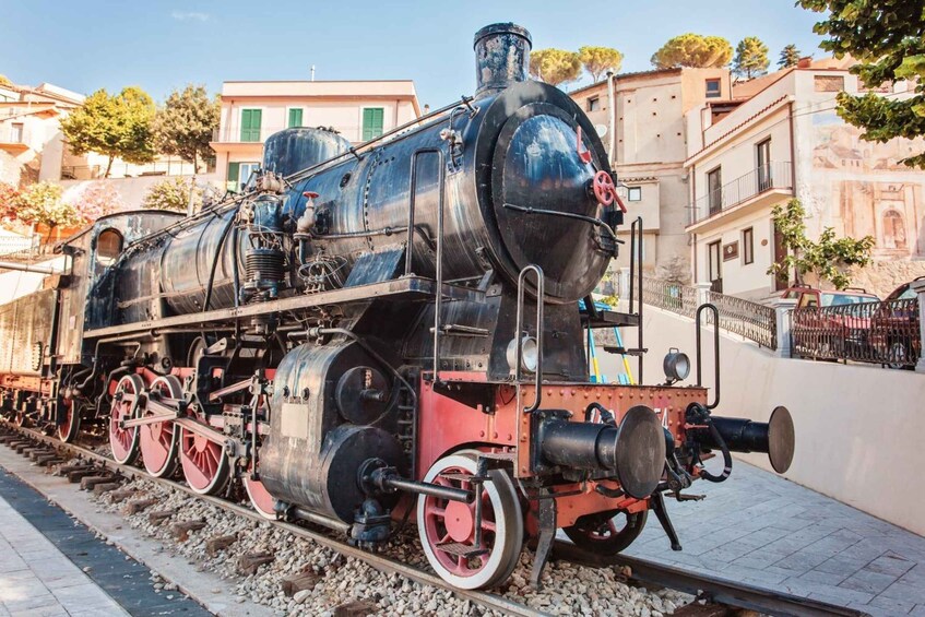 A steam locomotive on a track with buildings and trees in the background. 2