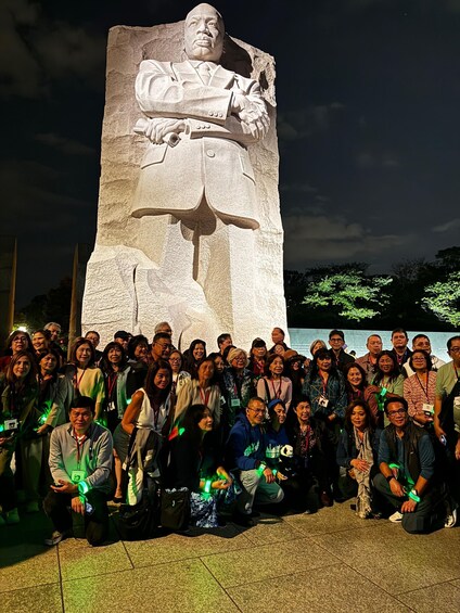 A large stone monument with a seated figure, surrounded by a group of people. 2