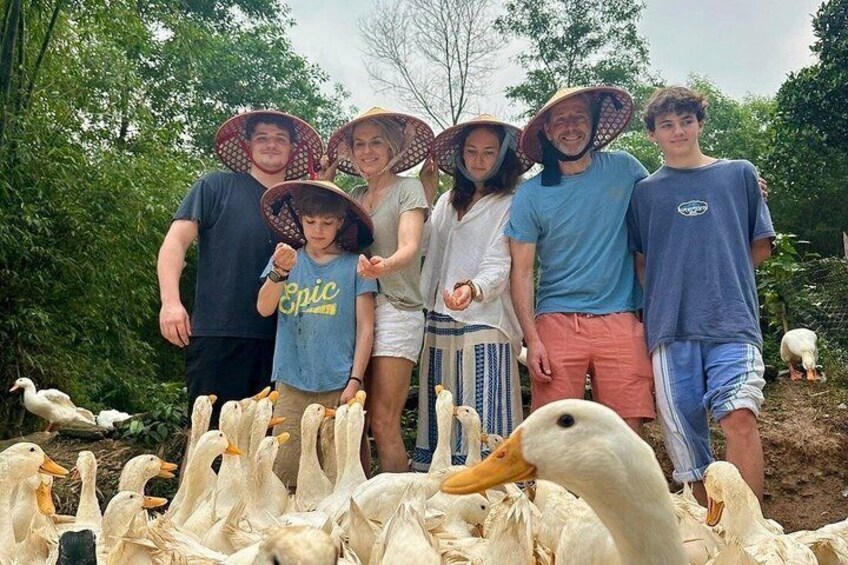 A group of people standing with ducks in a natural setting. 2