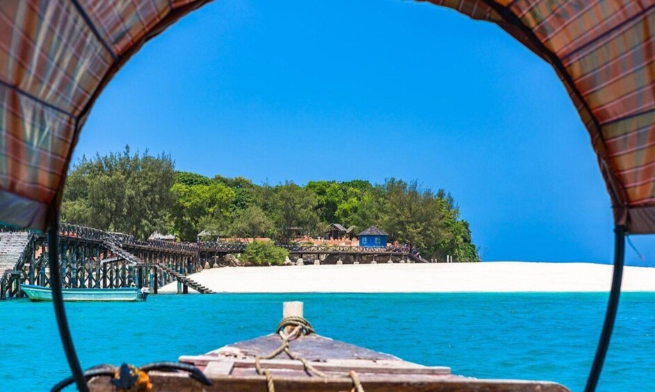 A boat with a view of a white sandy beach, a wooden pier, and a forested island. 5