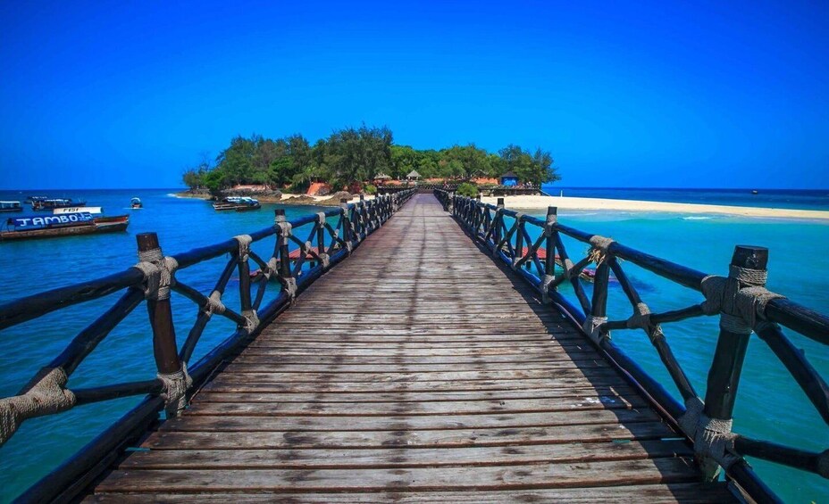 A wooden pier leading to a tropical island with boats docked nearby. 2