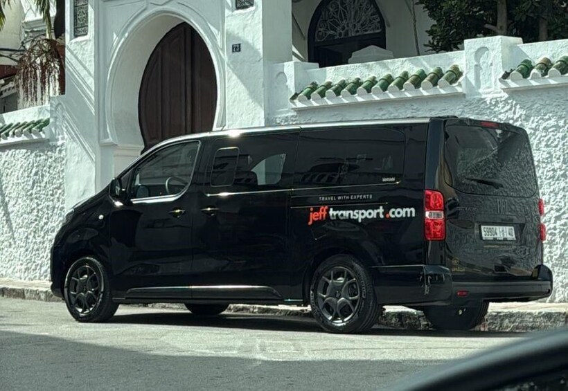 A black van parked in front of a white building with a large arched doorway. 2