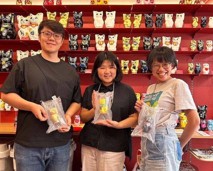 Three people holding small packaged items in front of a shelf with various cat-shaped objects. 3
