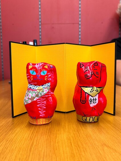 Two red cat figurines with Japanese characters on a wooden surface. 4