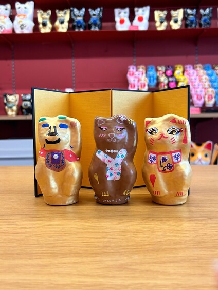 Three Maneki-neko figurines on a table with a red background. 2
