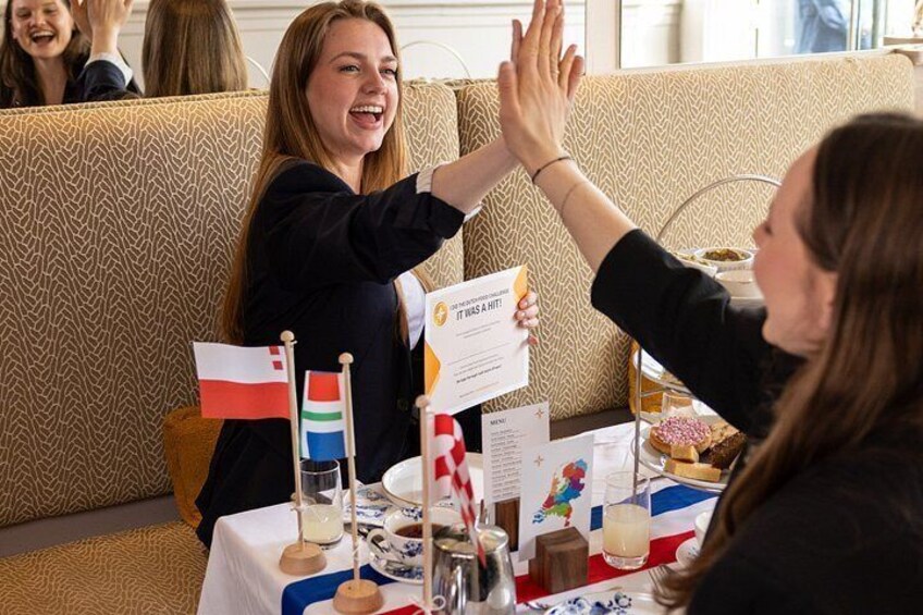 A group of people sitting at a table with a cake and flags, engaged in a high-five gesture. 4
