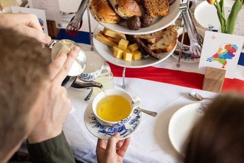 A person pouring tea into a cup, a plate with bread and cheese, and a table with a red and white tablecloth. 5