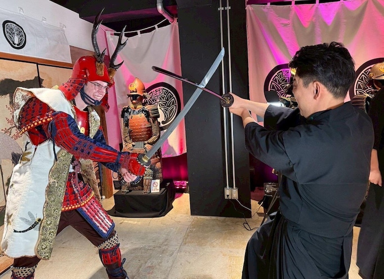 A person in a samurai costume with a sword, another person aiming a bow, and a samurai armor display in the background. 1