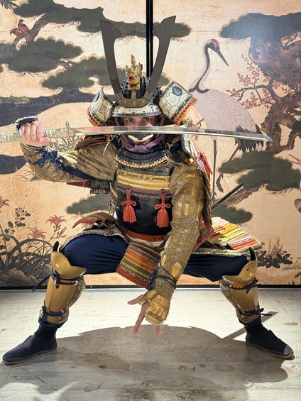 A person in a samurai costume with a sword, standing in front of a mural. 2