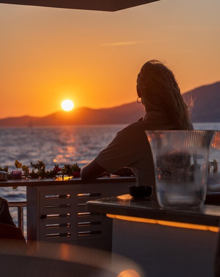 A person sitting at a table with a glass of water, overlooking a sunset over the ocean. 1