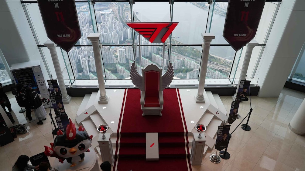 A gaming chair with a red backrest and a logo, surrounded by promotional banners and a trophy. 5