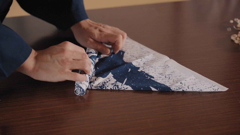 Hands folding a piece of paper with a blue and white pattern. 4