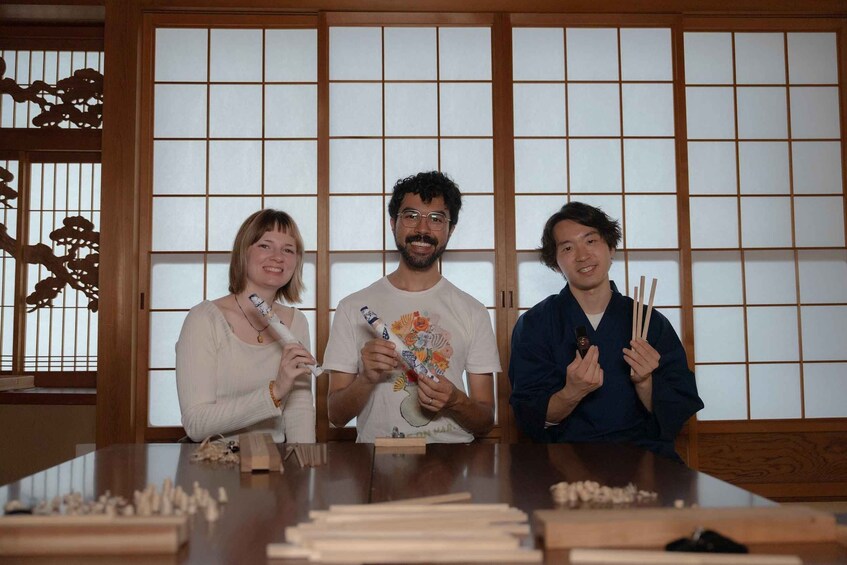 Three people sitting at a table with chopsticks and wooden blocks, in a room with traditional Japanese sliding doors. 2