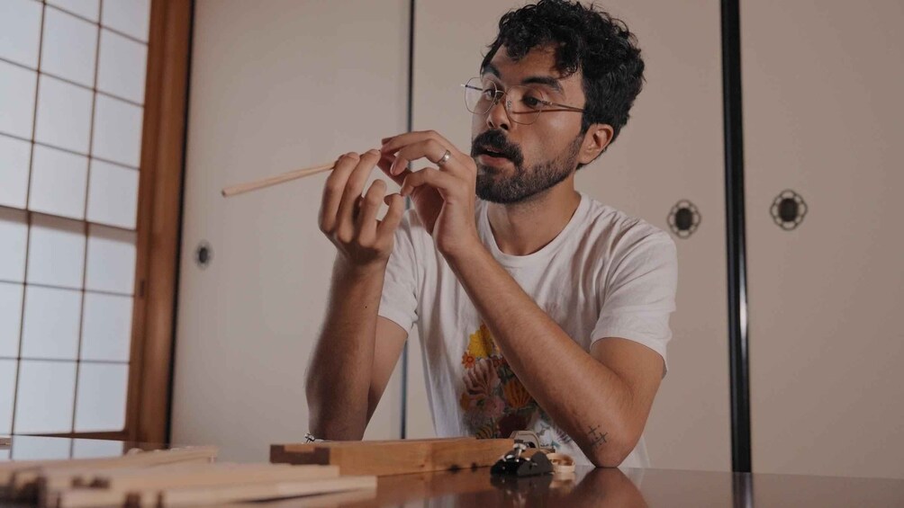 A person sitting at a table with chopsticks, wearing a white t-shirt with a graphic design. 5