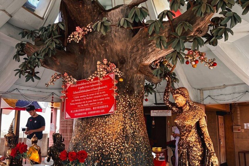 A large tree with a golden statue, a red sign, and red flowers. 2