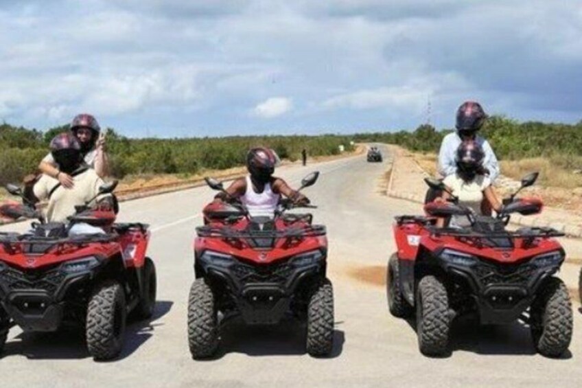 Three people on ATVs on a paved road with vegetation on the sides. 3
