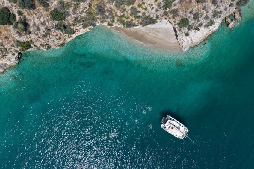 Vista aérea de un barco en aguas turquesas cerca de una playa arenosa con terreno rocoso. 2