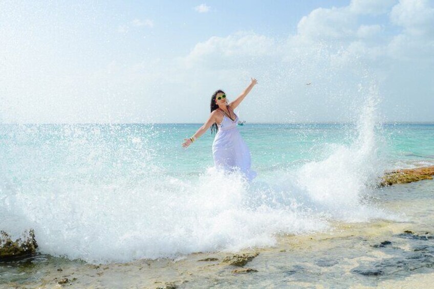 A person in a white dress standing in shallow water with waves crashing around them. 1